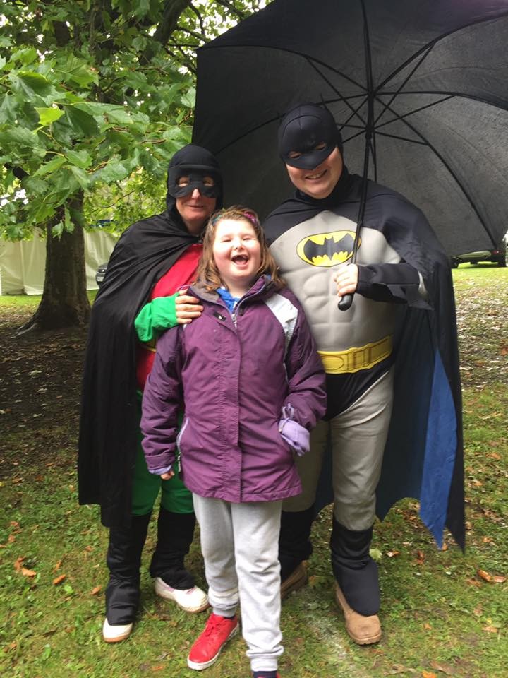 Batman and Robin pose with a young girl in the rain with a umberella
