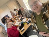This is image is of the craft and chat group, is show a group of people  round a table crafting with one person taking the photo